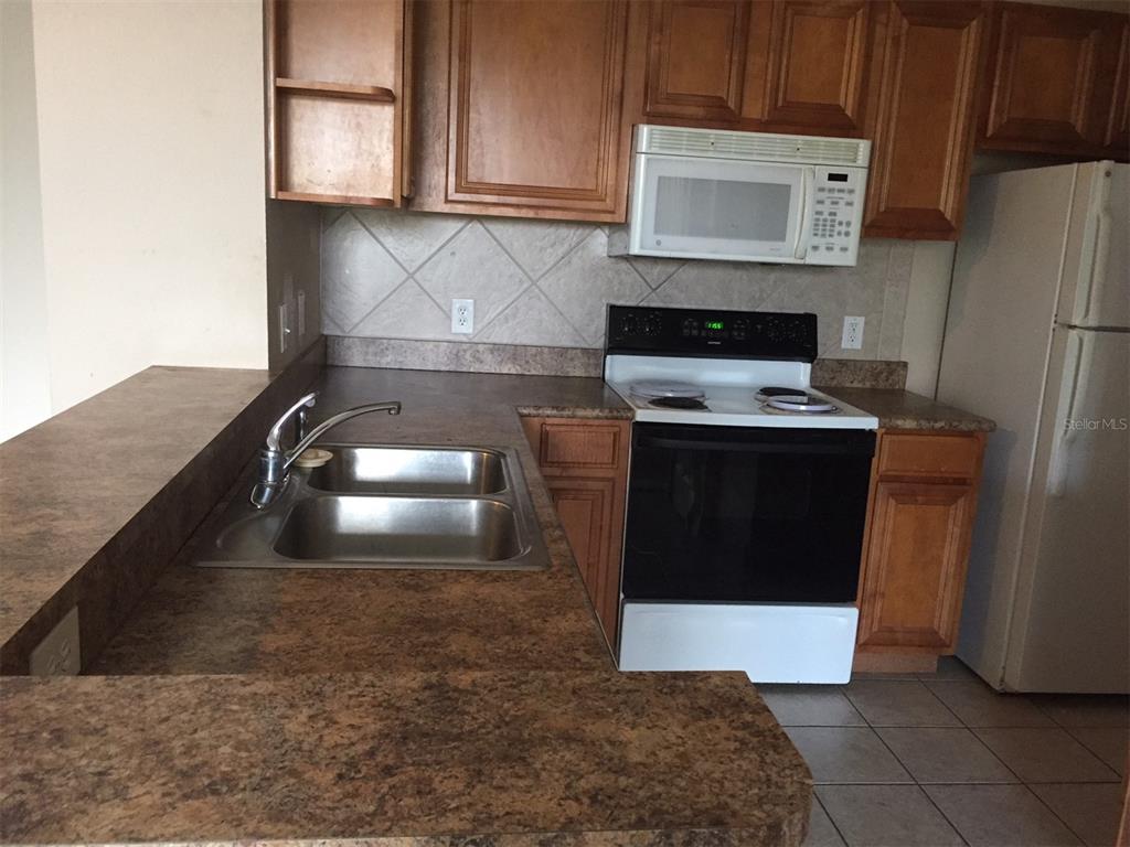 A kitchen features wood cabinets, a double-basin sink, a white stove, and a white refrigerator — 5572 METROWEST BOULEVARD UNIT 5-209, ORLANDO, FL