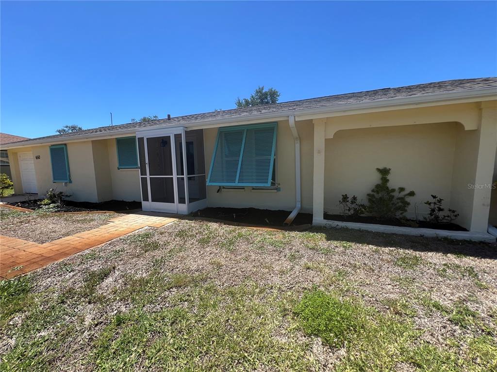 A single-story house with yellow stucco walls, teal shutters, and a screened front entryway — 650 HARTFORD DRIVE NW, PORT CHARLOTTE, FL