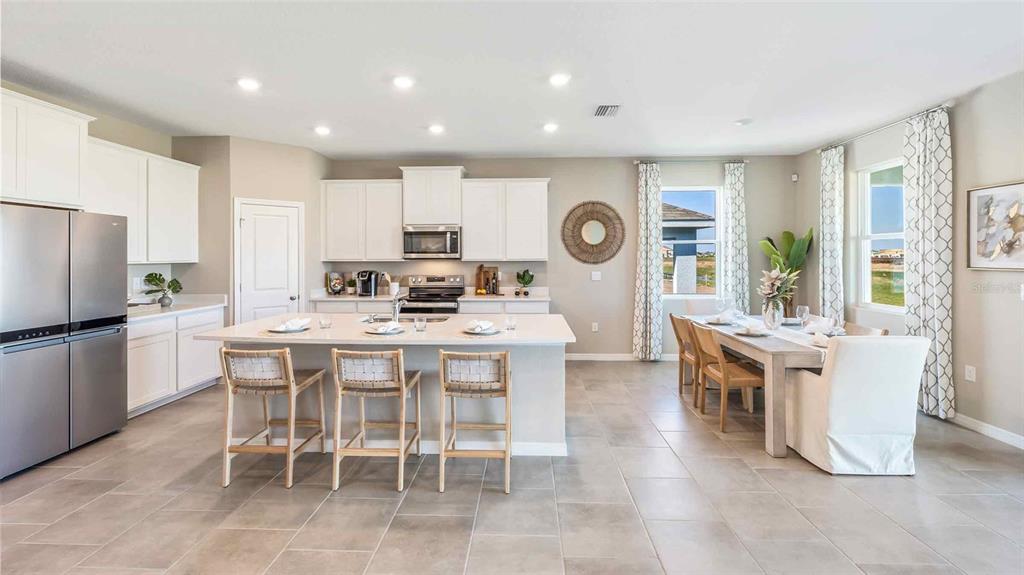 A bright kitchen features white cabinets, a large island with three stools, and a dining area — 3503 HARVEST GARDENS LOOP, PLANT CITY, FL