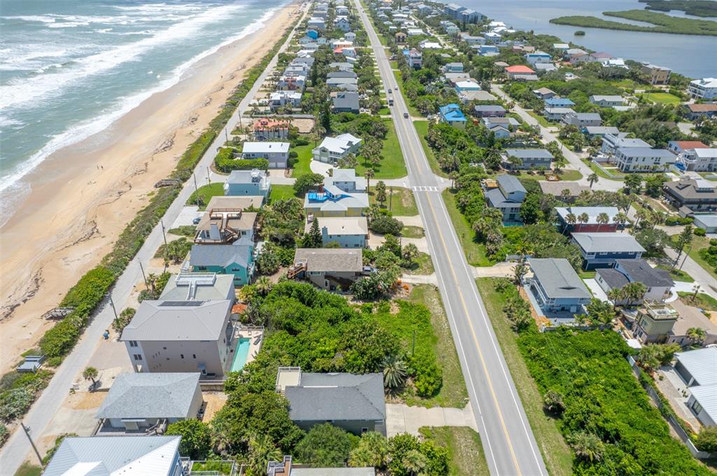An aerial view shows a coastal road lined with houses between the ocean and a bay — 6371 TURTLEMOUND ROAD, NEW SMYRNA BEACH, FL