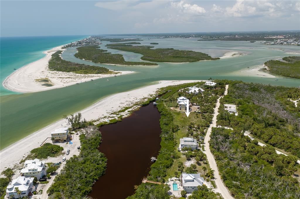 An aerial view shows a coastal property with a house, a pond, and beach access — 6060 RUM COVE DRIVE, PLACIDA, FL