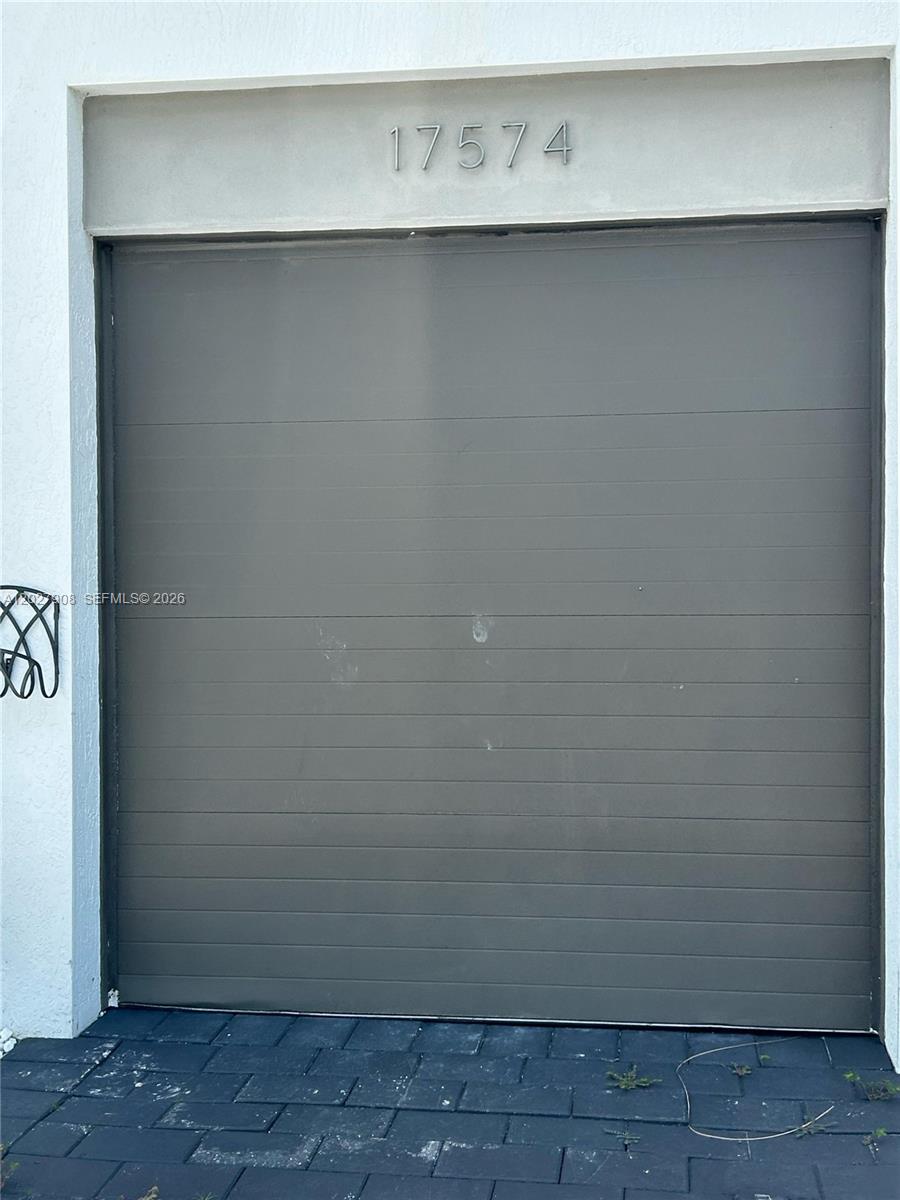 A dark gray garage door is set into a white exterior wall with the number 17574 — MIAMI, FL