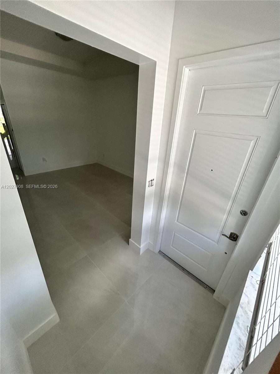 An entryway with a white door leads into a room with light-colored tile flooring — MIAMI, FL