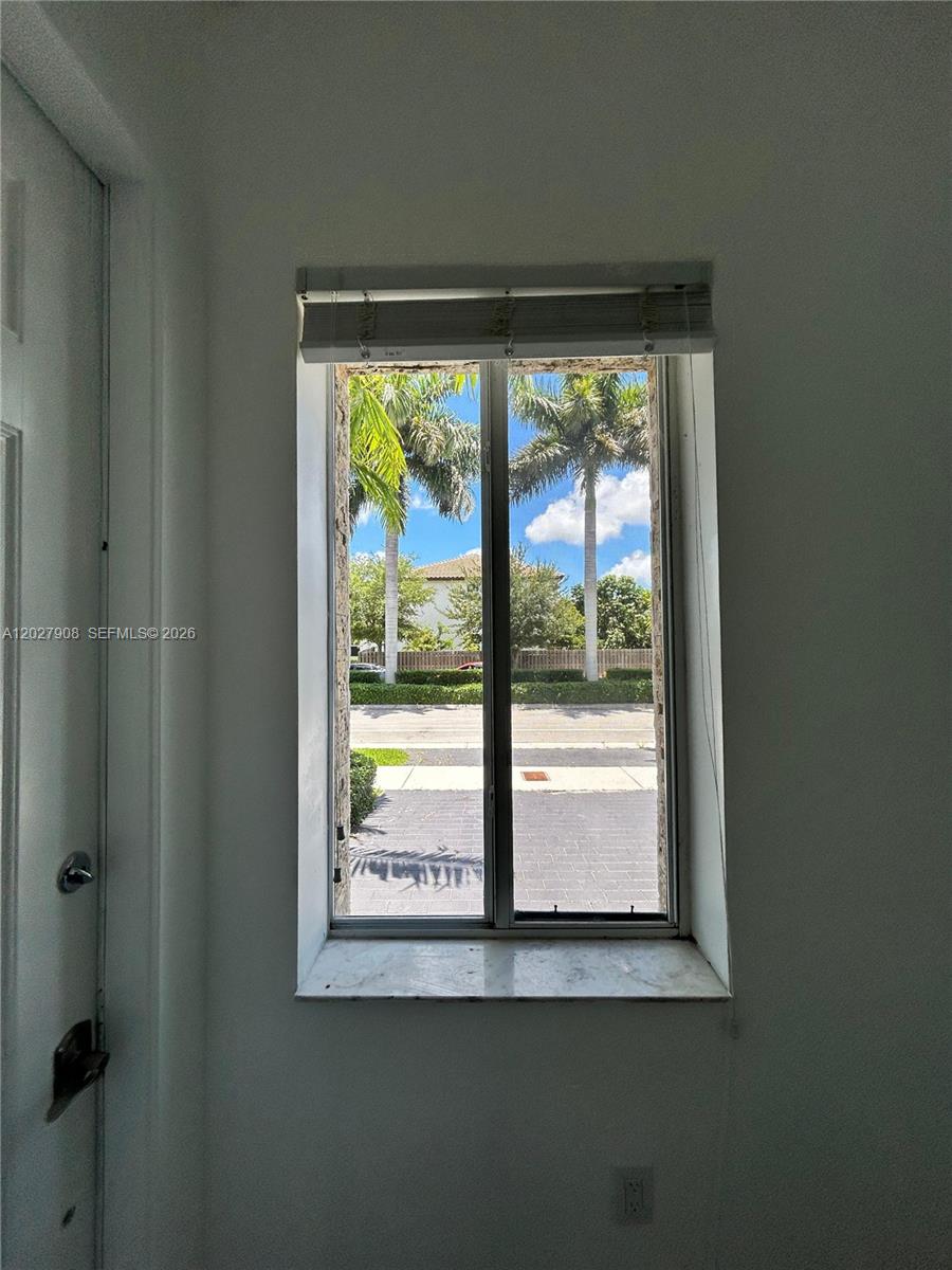 A window with a white frame and blinds overlooks a street with palm trees — MIAMI, FL