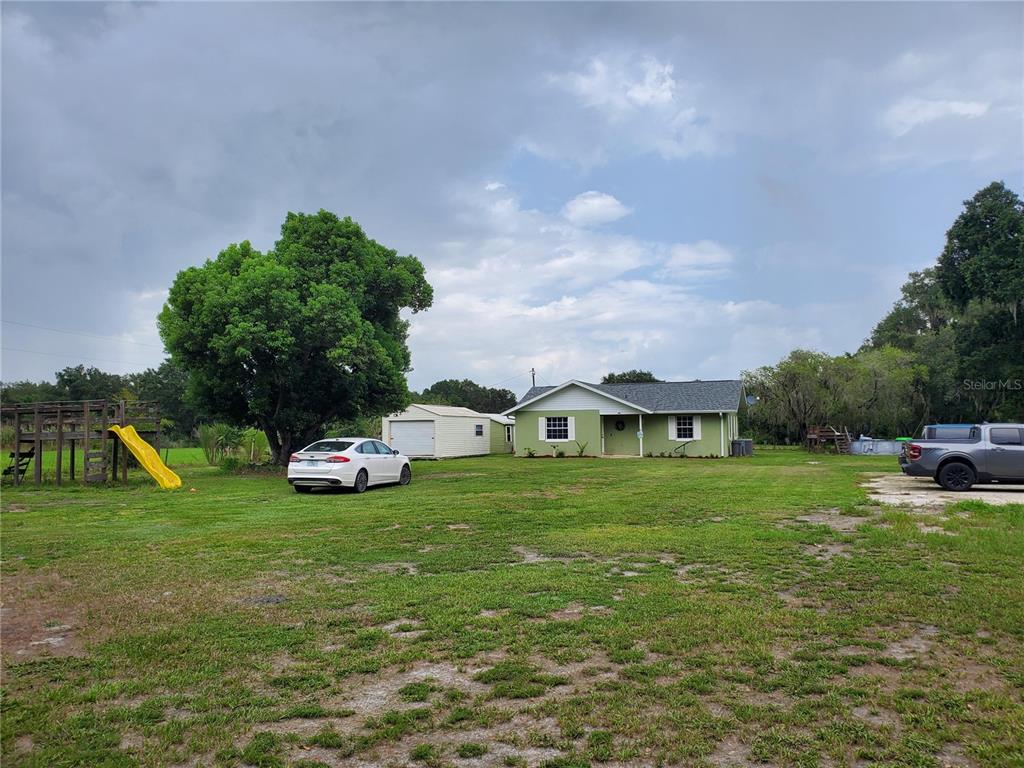 A light green house with a detached garage, a playground, and two cars parked outside — 1662 HARVILL ROAD, WAUCHULA, FL