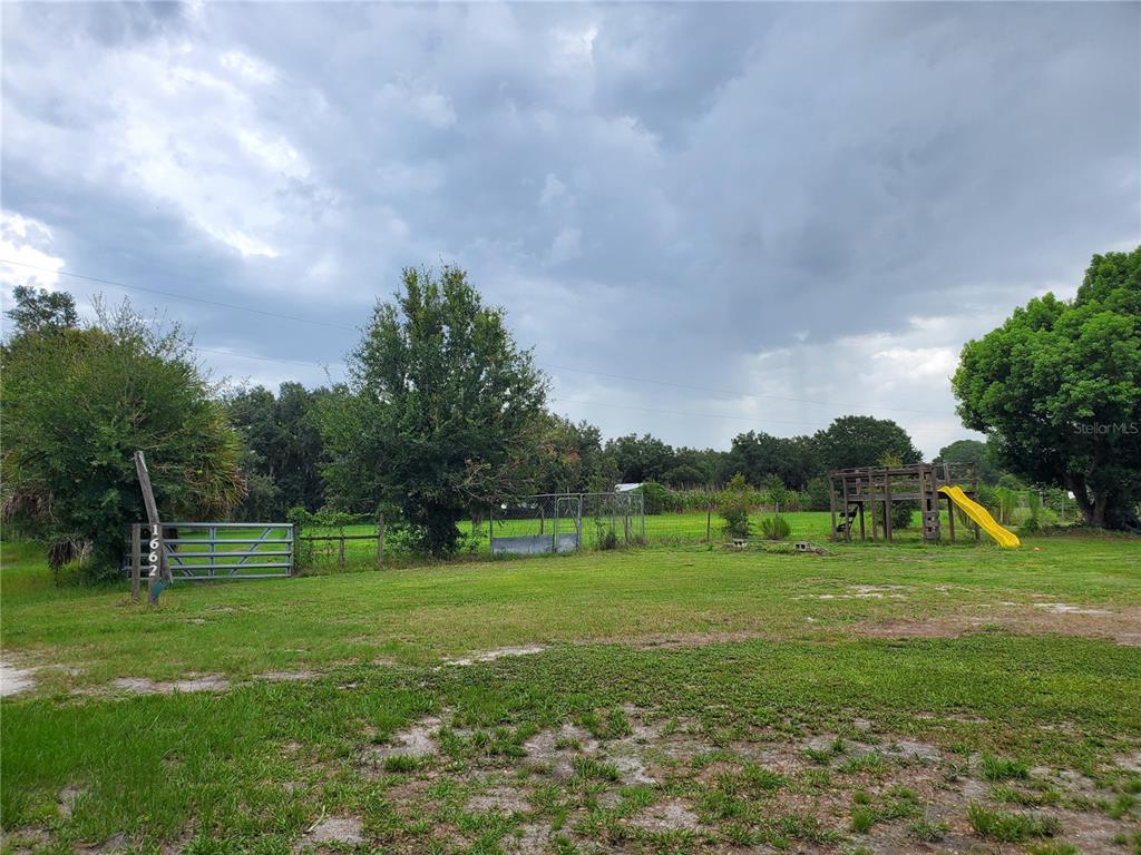 A grassy yard features a metal gate, a chain-link enclosure, and a wooden playground set — 1662 HARVILL ROAD, WAUCHULA, FL