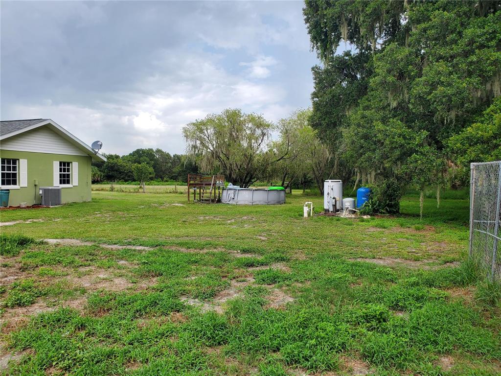 A green house stands beside a grassy yard featuring an above-ground pool and large trees — 1662 HARVILL ROAD, WAUCHULA, FL