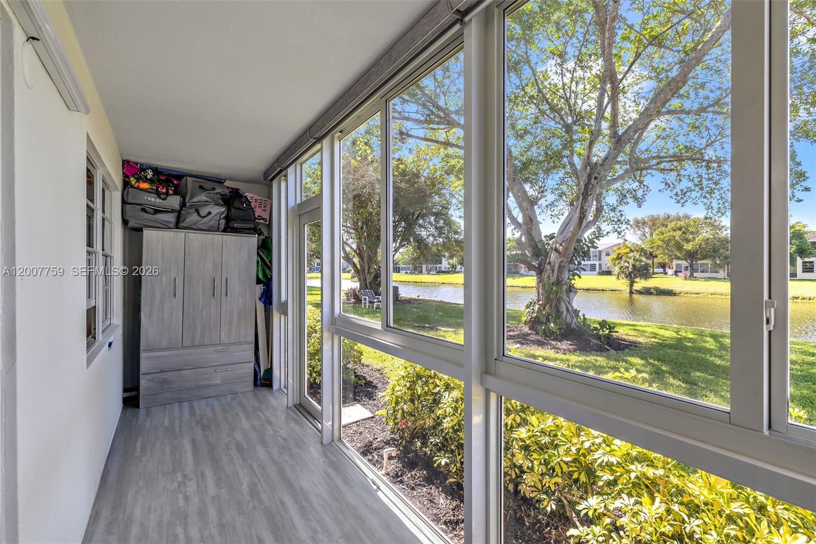 A sunroom features light wood-look flooring, a storage cabinet, and large windows overlooking a lake — 494 W Tilford  W # 494, Deerfield Beach FL 33442, DEERFIELD BEACH, FL