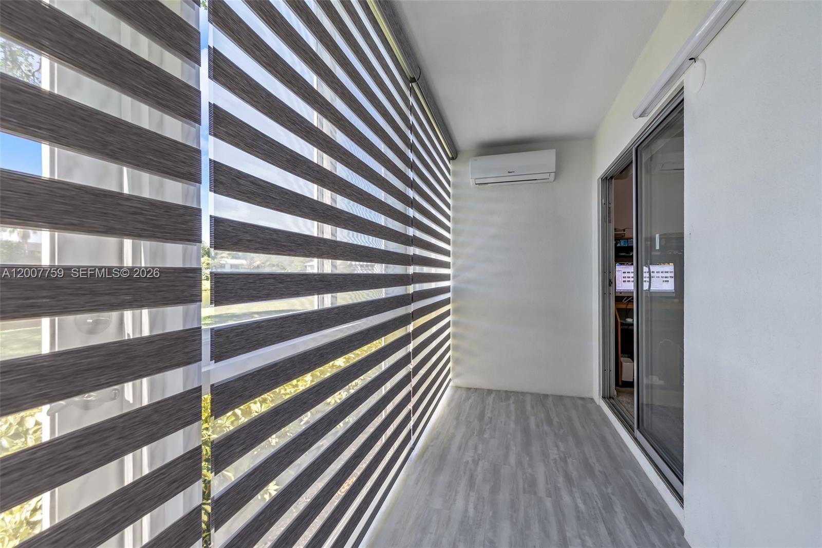 A narrow balcony features gray wood-look flooring, striped roller shades, and a wall-mounted air conditioner — 494 W Tilford  W # 494, Deerfield Beach FL 33442, DEERFIELD BEACH, FL
