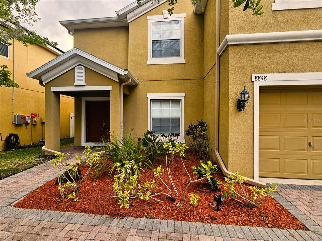 The exterior of a two-story yellow house features a paved driveway and a landscaped garden — 8848 CAMERON CREST DRIVE, TAMPA, FL