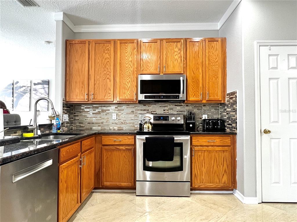 A kitchen features wood cabinets, stainless steel appliances, a mosaic tile backsplash, and dark countertops — 8848 CAMERON CREST DRIVE, TAMPA, FL