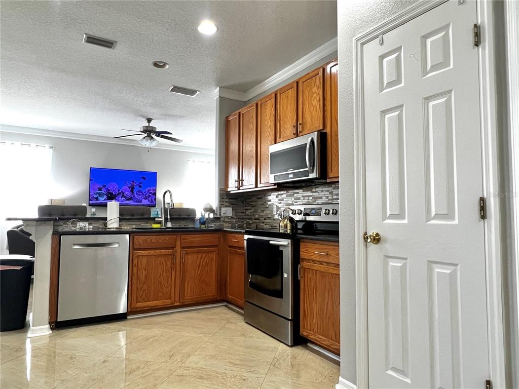 A kitchen features wood cabinets, stainless steel appliances, a tiled backsplash, and light-colored floor tiles — 8848 CAMERON CREST DRIVE, TAMPA, FL