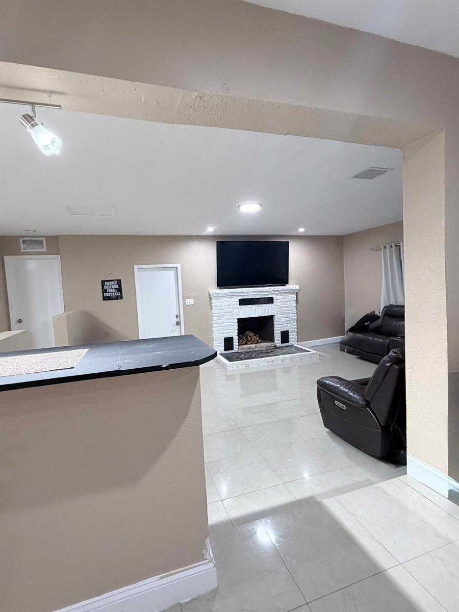 A living room features a white brick fireplace, a wall-mounted television, and tile flooring — 2000 SW 95th Terrace, Miramar FL 33025, MIRAMAR, FL
