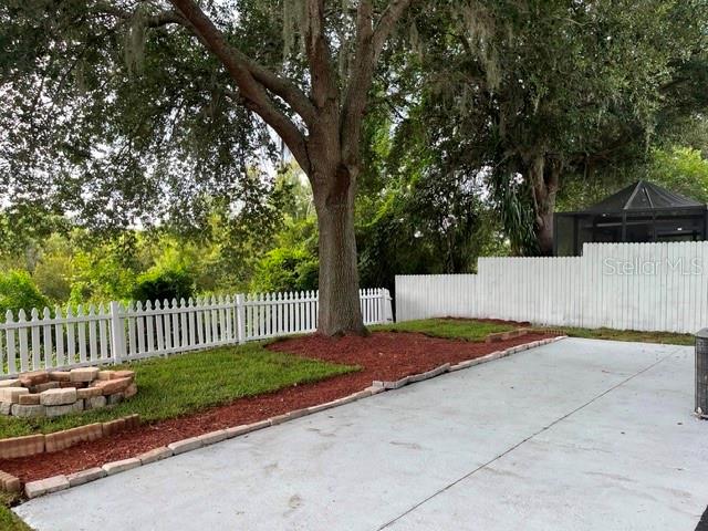 A concrete driveway leads to a white picket fence, a large tree, and a screened gazebo — 10036 PERTHSHIRE CIRCLE, LAND O LAKES, FL