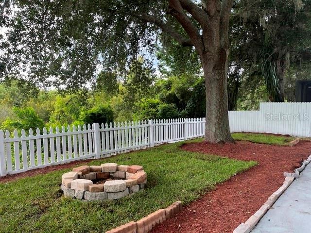 A backyard features a stone fire pit, a white picket fence, and a large tree — 10036 PERTHSHIRE CIRCLE, LAND O LAKES, FL