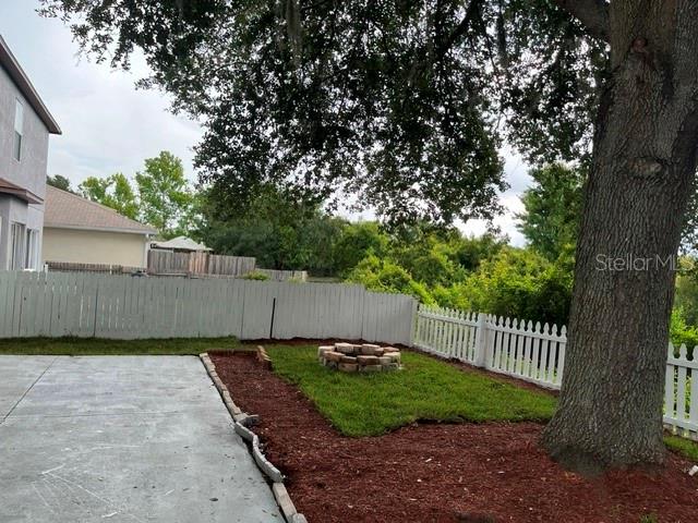 A backyard features a concrete patio, a small lawn with a fire pit, and white fencing — 10036 PERTHSHIRE CIRCLE, LAND O LAKES, FL