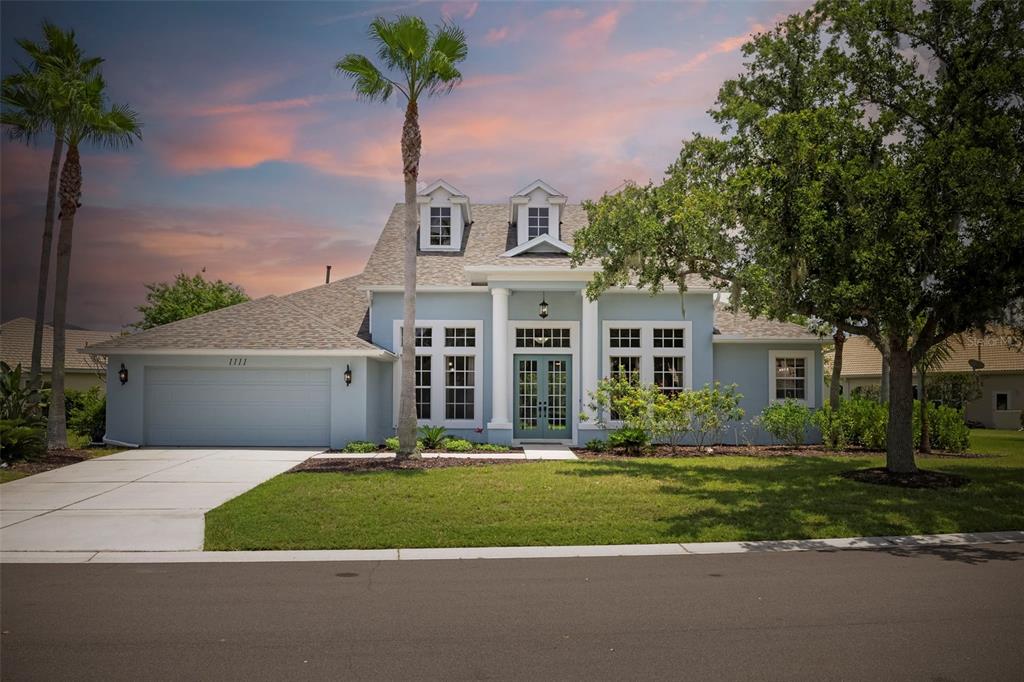A light blue single-story house with a two-car garage, palm trees, and a front porch — 1111 BRAMBLING COURT, BRADENTON, FL