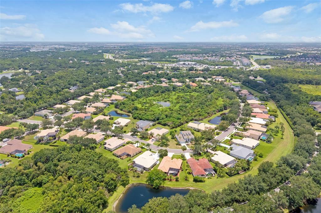 An aerial view shows a suburban neighborhood with houses surrounding a central wooded area — 1111 BRAMBLING COURT, BRADENTON, FL