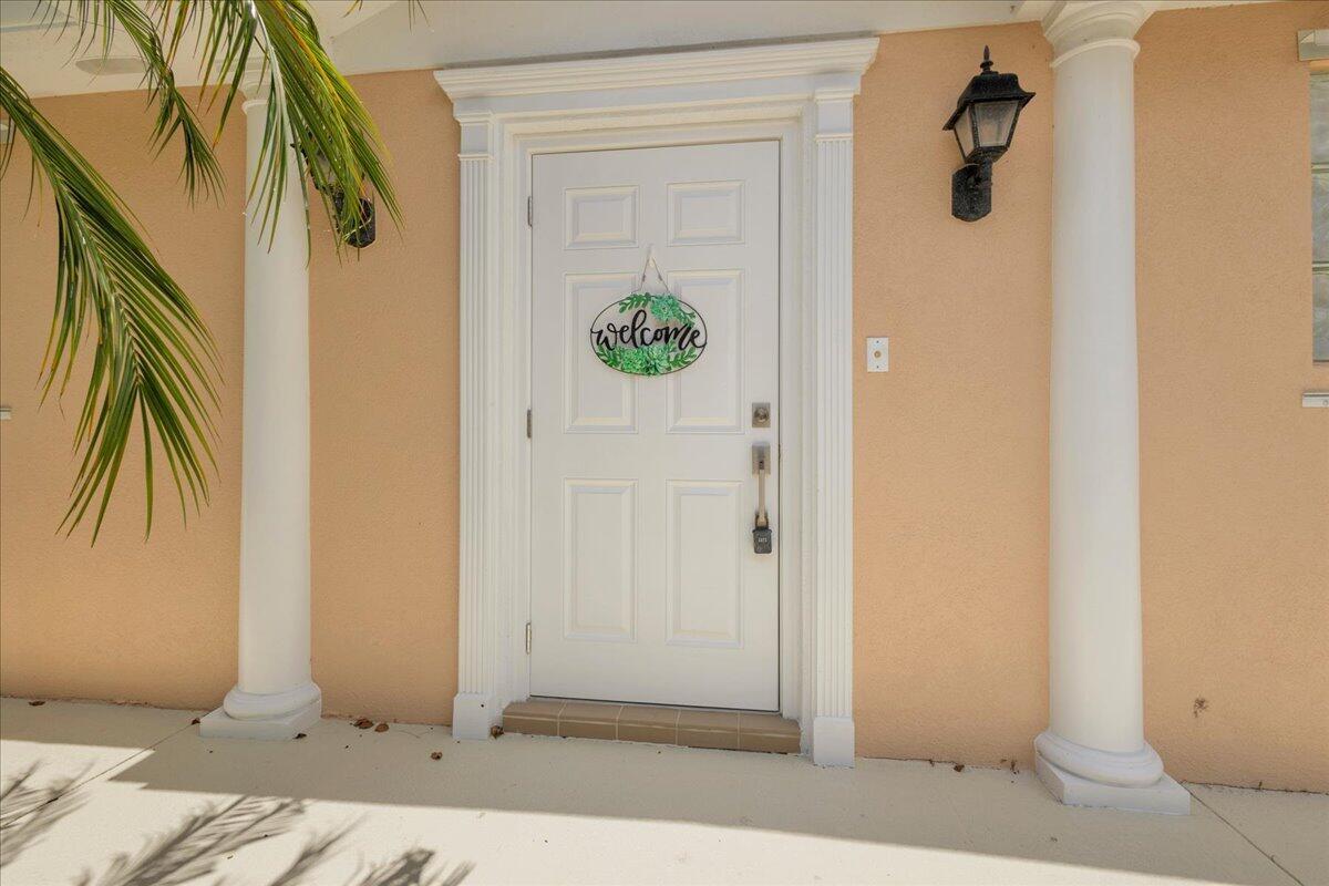 A white front door with a welcome sign is framed by two columns on a porch — 10882 SW Dardanelle Drive, FL 34987, FL