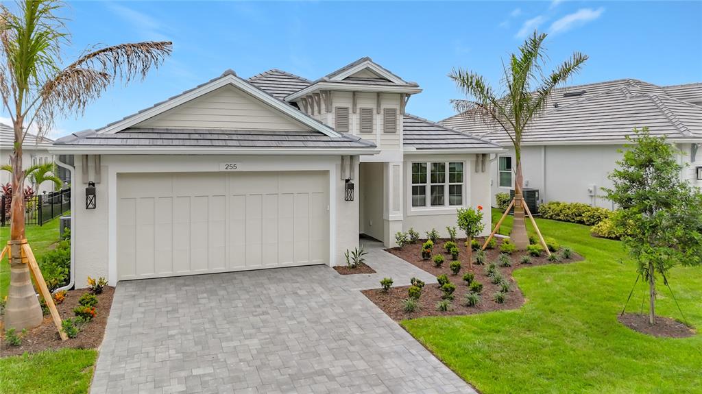 A single-story house with a beige stucco exterior, a gray tile roof, and a paver driveway — 255 MONET TRAIL, BRADENTON, FL