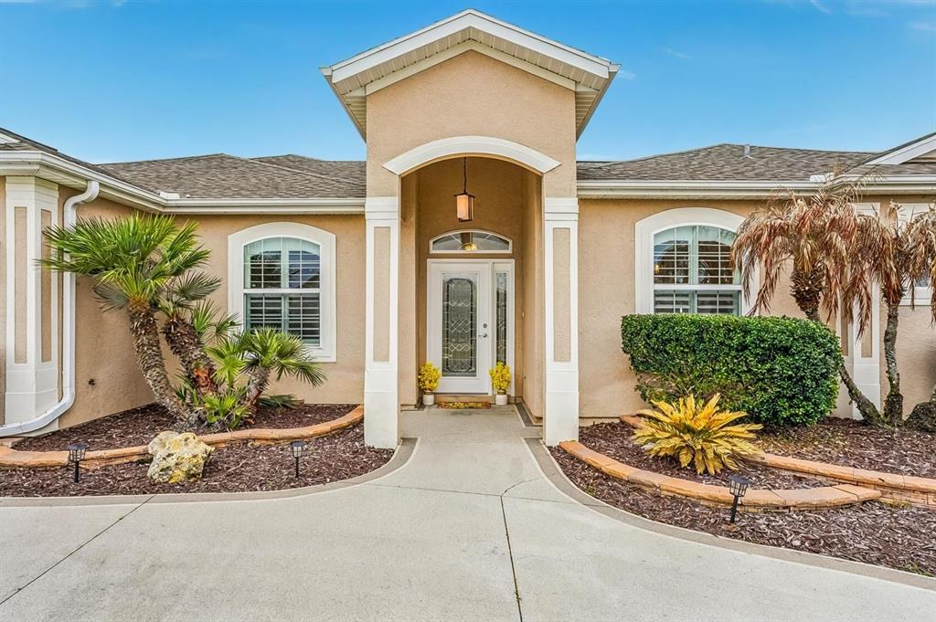 The exterior of a tan stucco house features a covered entryway and landscaped front yard — 12371 NE 48TH CIRCLE, OXFORD, FL