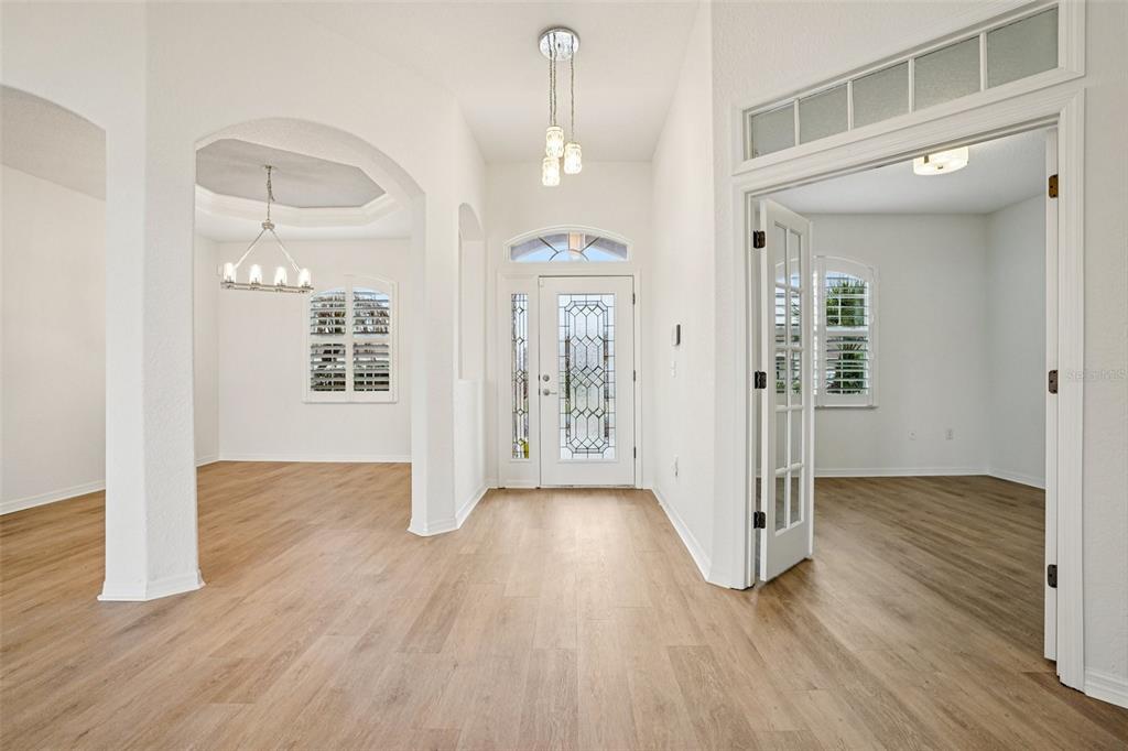 A bright foyer features light wood-look flooring, a glass-paneled front door, and arched entryways — 12371 NE 48TH CIRCLE, OXFORD, FL