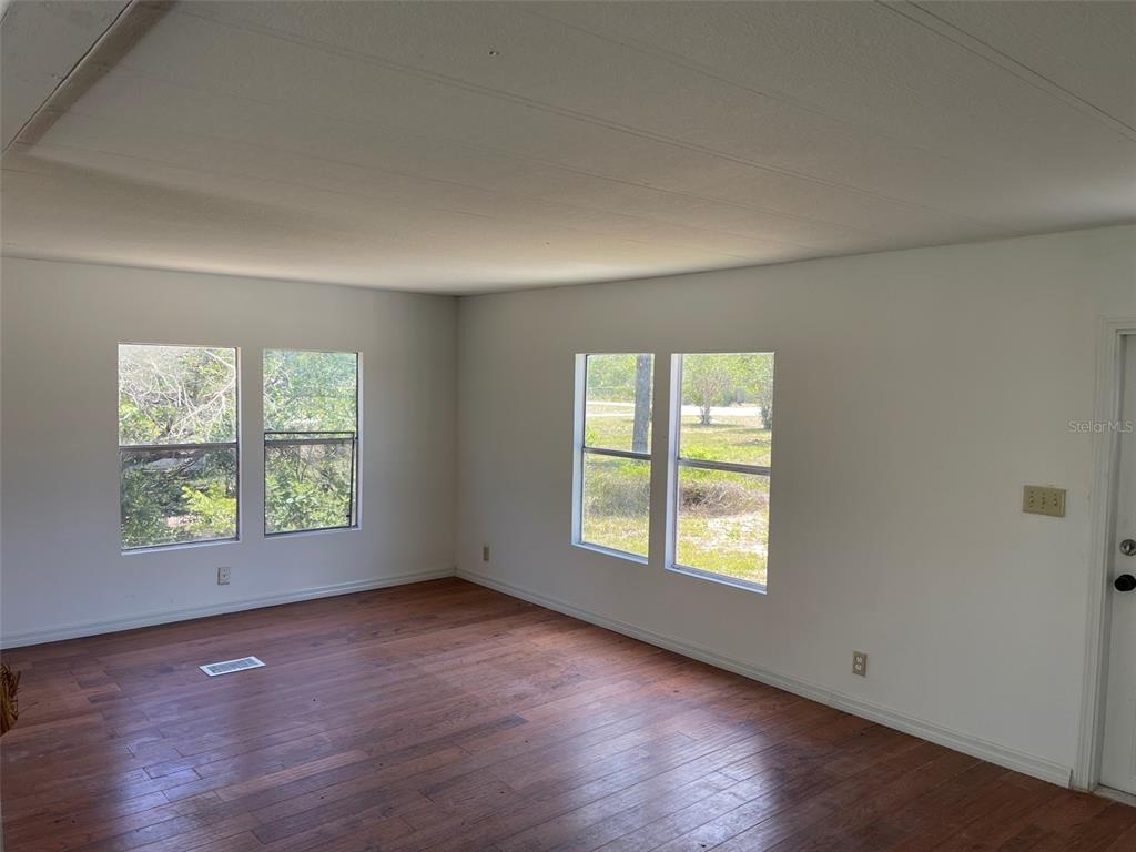 An empty room with white walls, wood-look flooring, and four windows overlooking a wooded area — 16329 CALDWELL LANE, SPRING HILL, FL