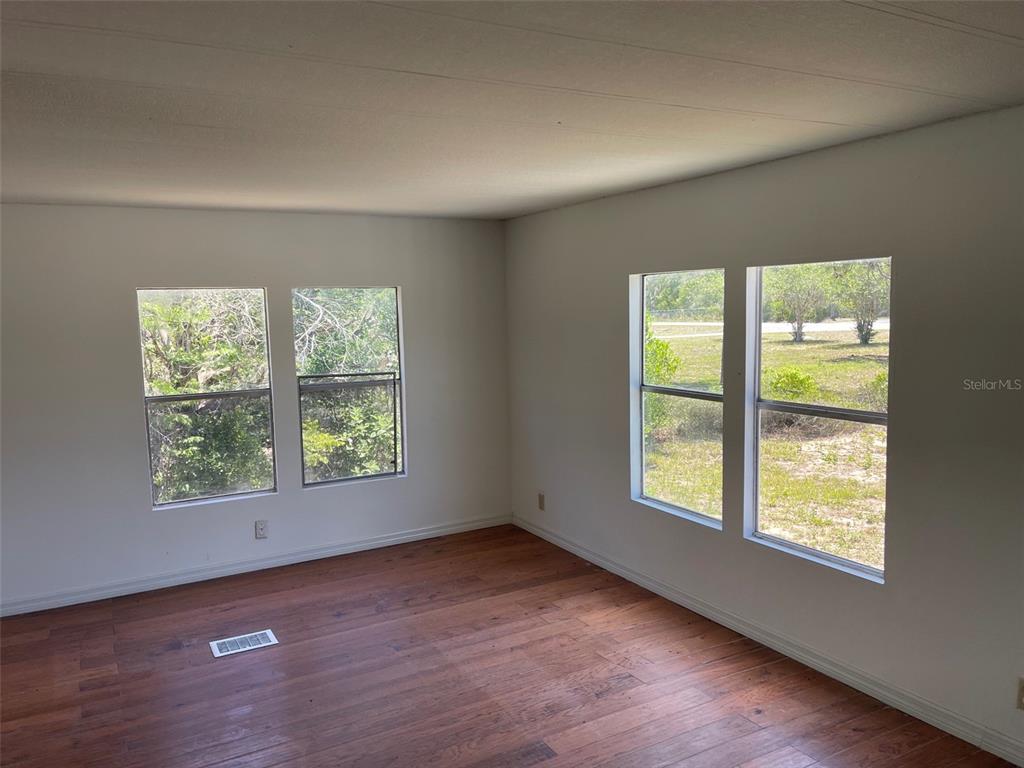 An empty room with wood-look flooring, white walls, and four windows overlooking a grassy yard — 16329 CALDWELL LANE, SPRING HILL, FL