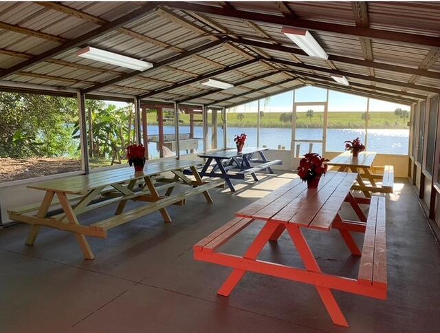 A screened-in pavilion features multiple picnic tables overlooking a lake and grassy landscape — 8680 Us Highway 441 SE, Okeechobee FL 34974, OKEECHOBEE, FL