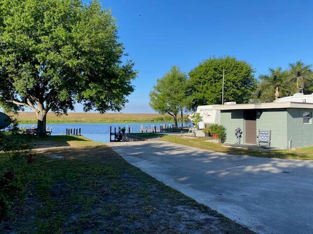 A concrete driveway leads toward a small house and a trailer near a waterfront dock — 8680 Us Highway 441 SE, Okeechobee FL 34974, OKEECHOBEE, FL