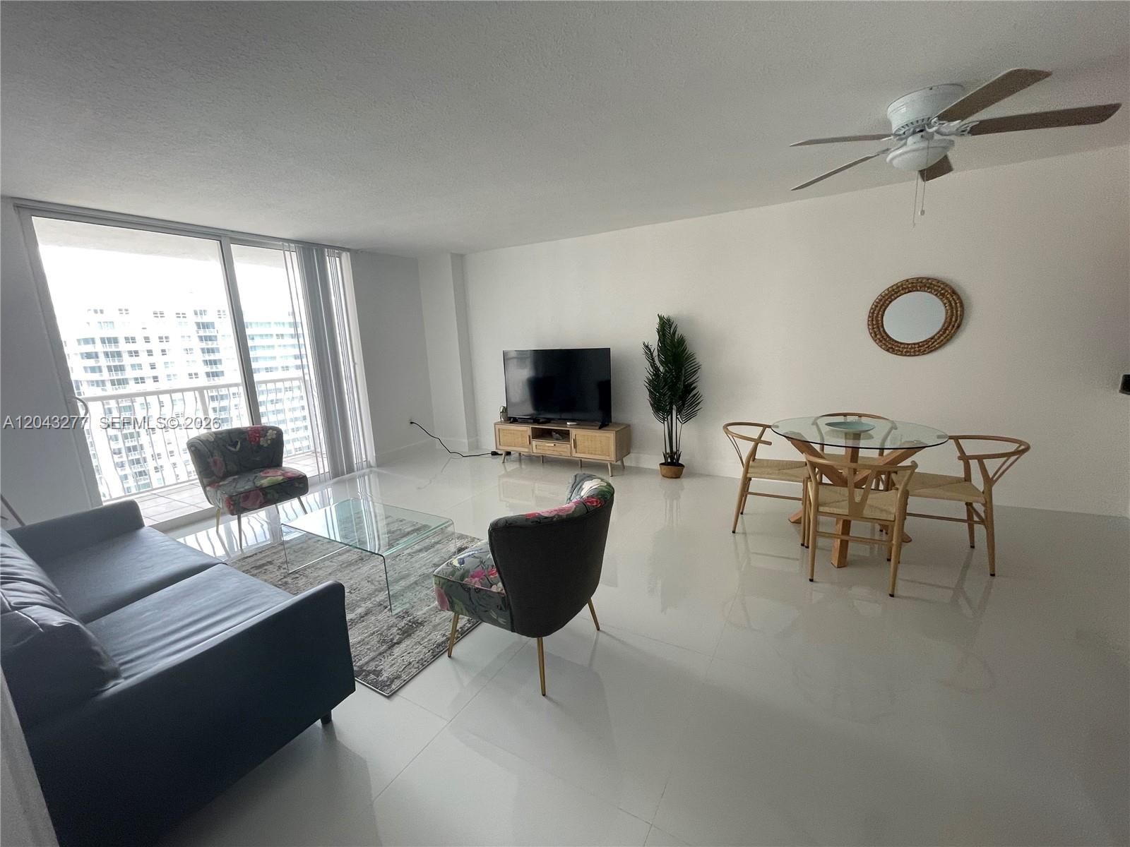 A living and dining area features white tile floors, a glass coffee table, and balcony access — 1200 BRICKELL BAY DR # 3104, Miami FL 33131, MIAMI, FL