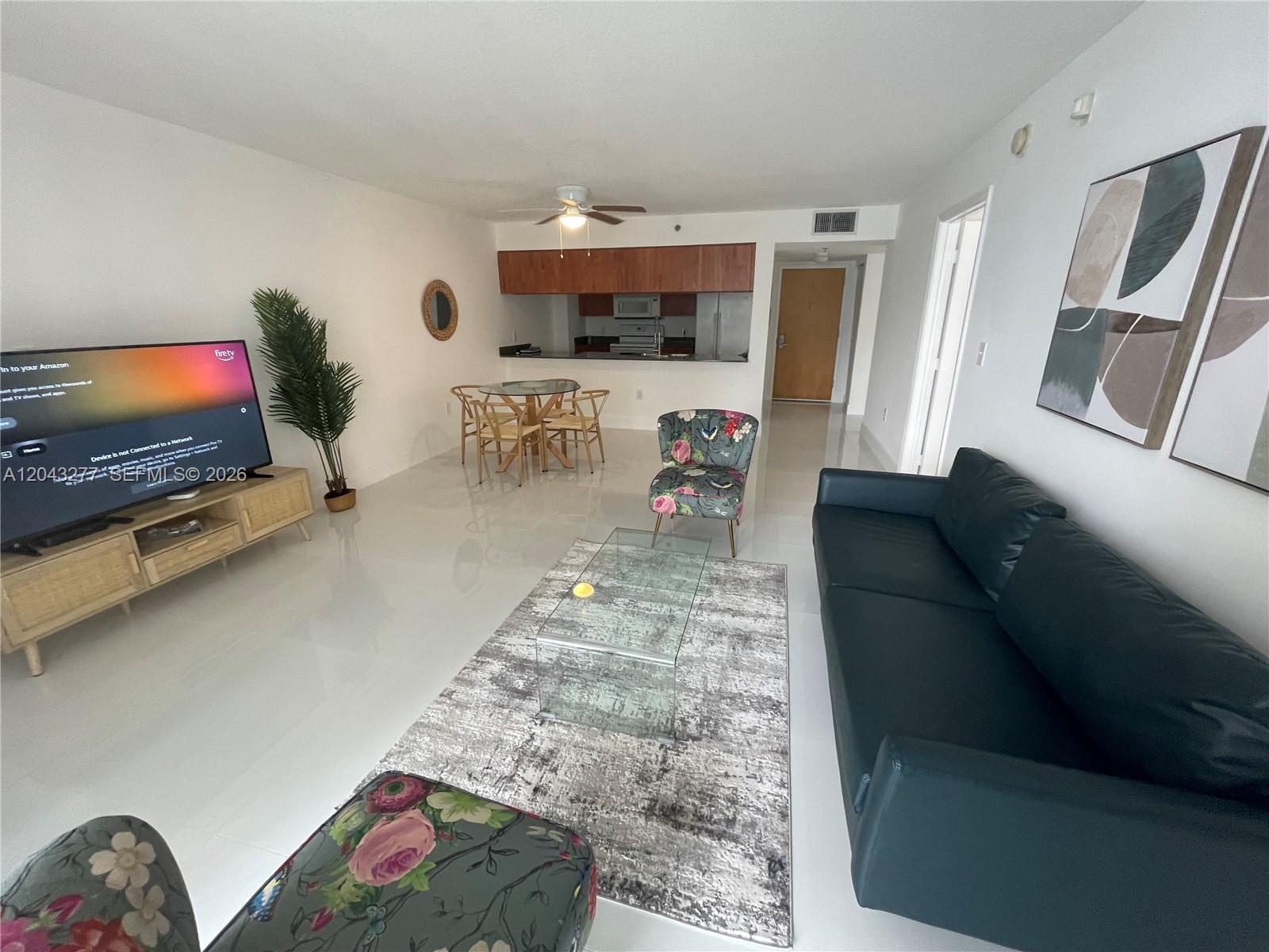 A living room with a black sofa, glass coffee table, floral chairs, and an open kitchen — 1200 BRICKELL BAY DR # 3104, Miami FL 33131, MIAMI, FL