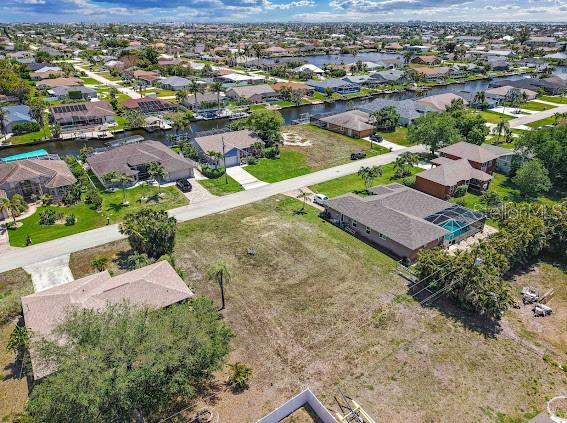 An aerial view shows a residential neighborhood with houses, a vacant lot, and canals — 4406 SW 5TH PLACE, CAPE CORAL, FL