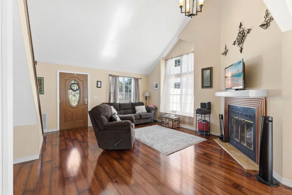 A living room with vaulted ceilings, hardwood floors, a fireplace, and a front entrance door — 2640 WAYMEYER DRIVE, ORLANDO, FL