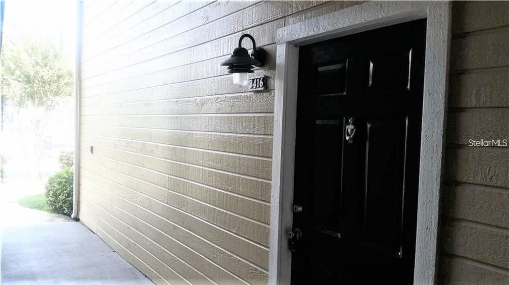 A black front door with a house number and light fixture on a tan wall — 1049 S HIAWASSEE ROAD UNIT 3416, ORLANDO, FL