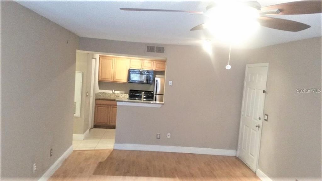 A living room with light wood flooring leads to an open kitchen with wooden cabinets — 1049 S HIAWASSEE ROAD UNIT 3416, ORLANDO, FL