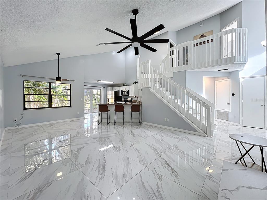 A bright living area features white marble-look tile flooring, a staircase, and a kitchen island — 622 ANHINGA ROAD, WINTER SPRINGS, FL