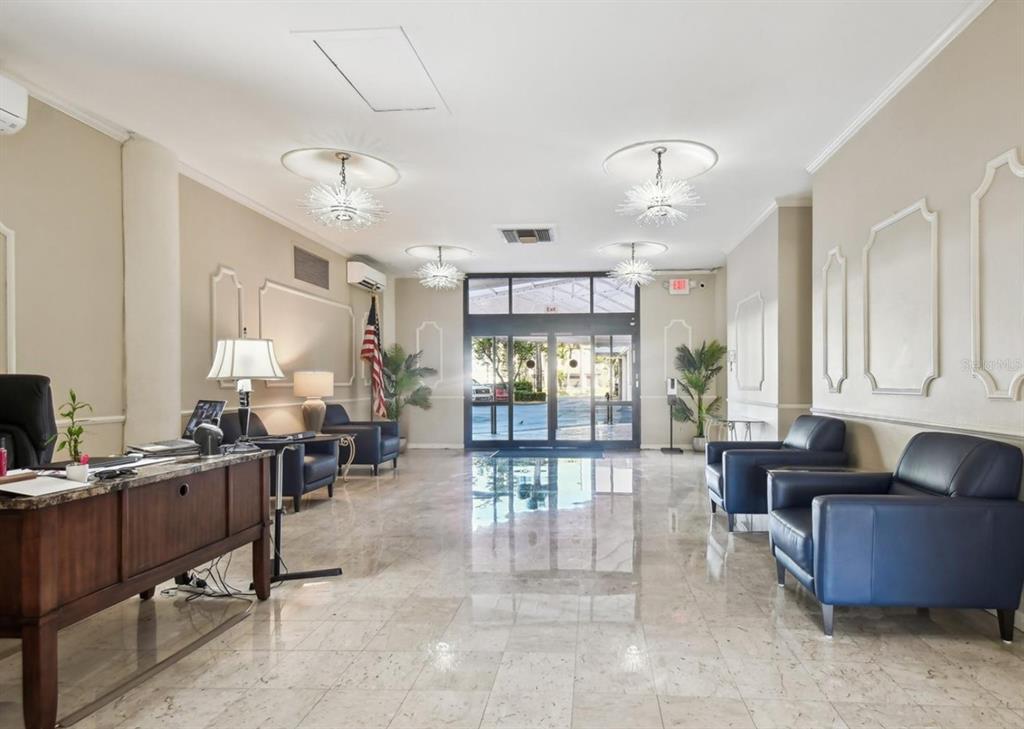 A bright lobby features a reception desk, blue leather armchairs, marble floors, and starburst chandeliers — 10355 PARADISE BOULEVARD UNIT 702, TREASURE ISLAND, FL