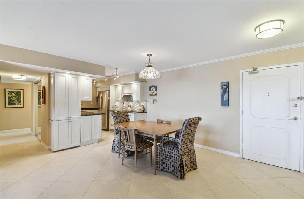 A dining area with a wooden table, patterned chairs, and an adjacent kitchen with white cabinets — 10355 PARADISE BOULEVARD UNIT 702, TREASURE ISLAND, FL