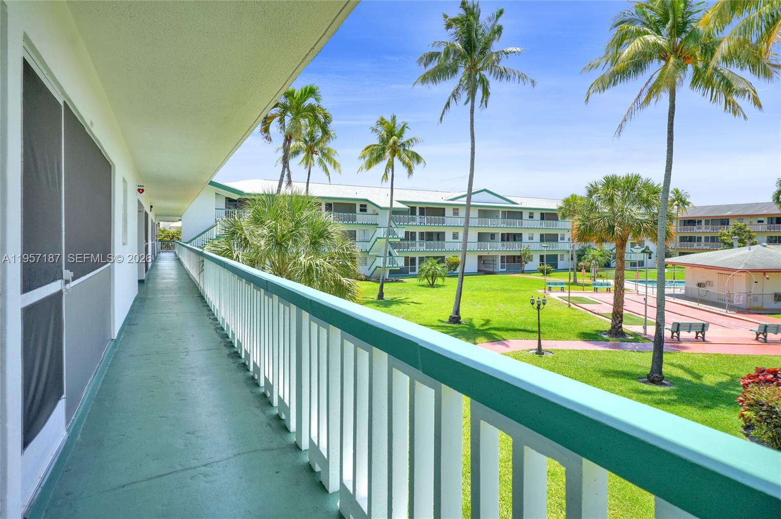 An outdoor walkway overlooks a grassy courtyard with palm trees and a swimming pool area — 5300 Washington St # I205, Hollywood FL 33021, HOLLYWOOD, FL