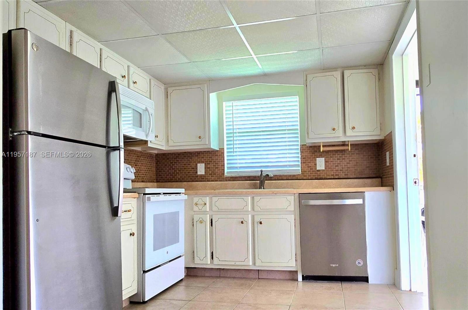 A kitchen features white cabinets, stainless steel appliances, a tiled backsplash, and light-colored floor tiles — 5300 Washington St # I205, Hollywood FL 33021, HOLLYWOOD, FL