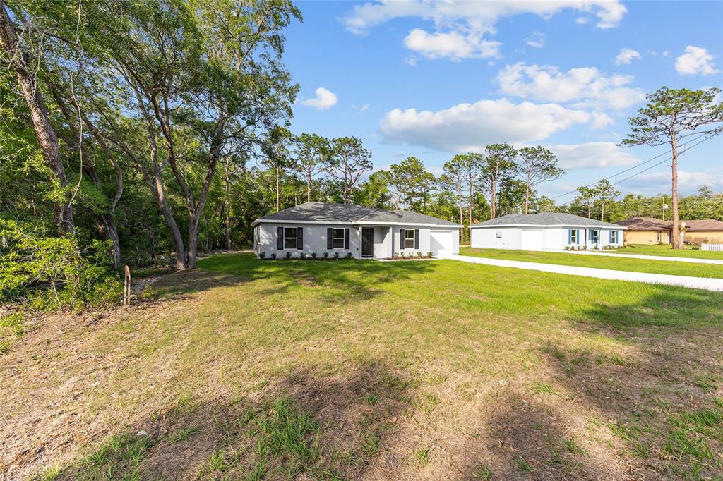 A single-story house with a white exterior and a driveway sits on a grassy lot — 358 LOCUST ROAD, OCALA, FL