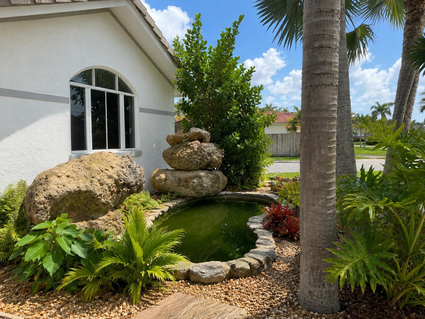 A small pond with a rock fountain sits in a landscaped garden beside a house — 17202 SW 149th Place, Miami FL 33187, MIAMI, FL
