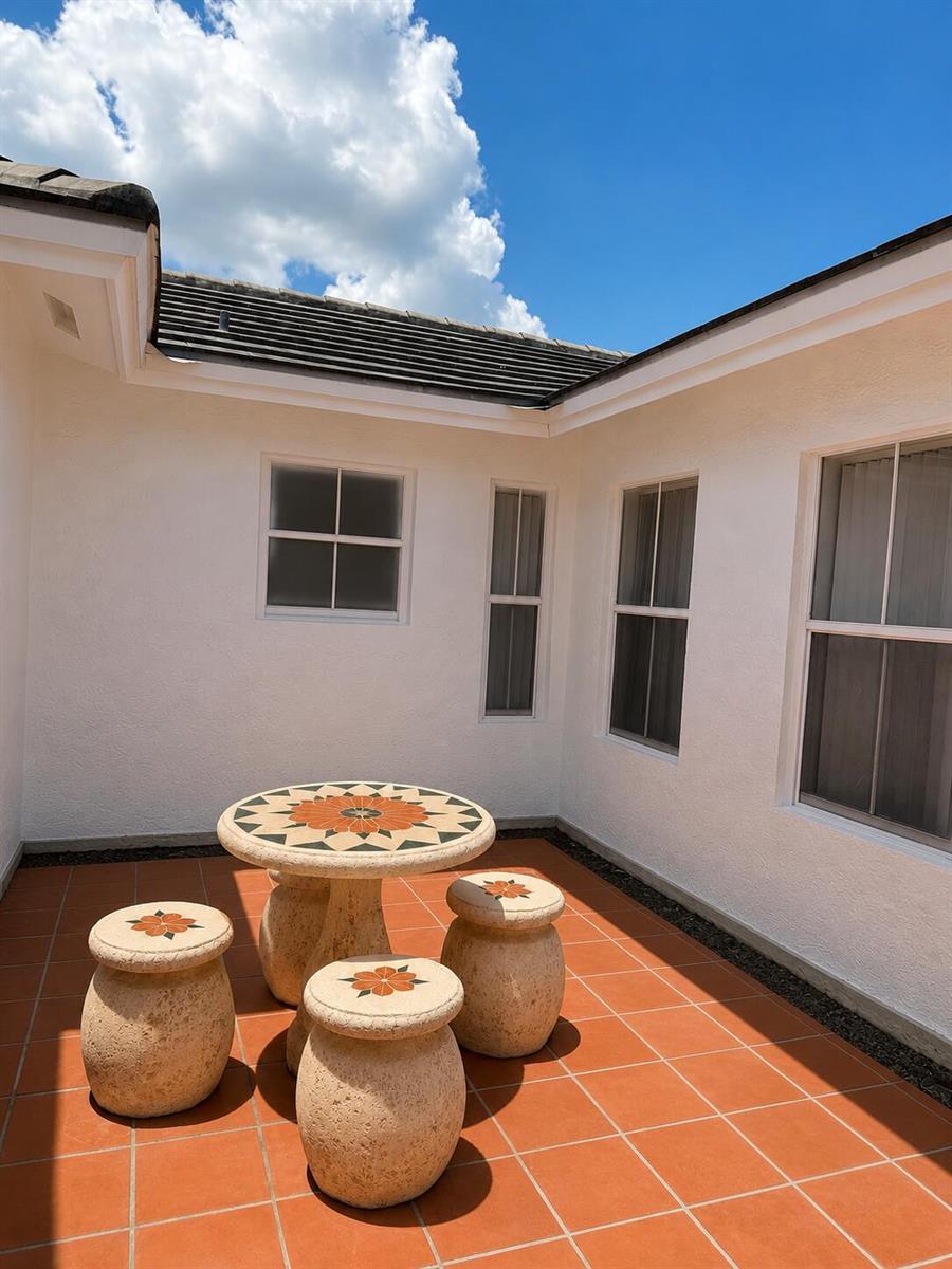 A stone patio set sits on a tiled courtyard outside a white stucco house — 17202 SW 149th Place, Miami FL 33187, MIAMI, FL