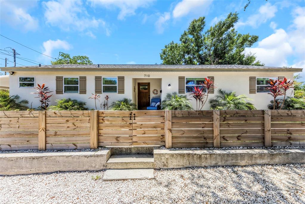 A single-story house with a wooden fence and gravel yard under a blue sky — 710 31ST AVENUE N, ST PETERSBURG, FL