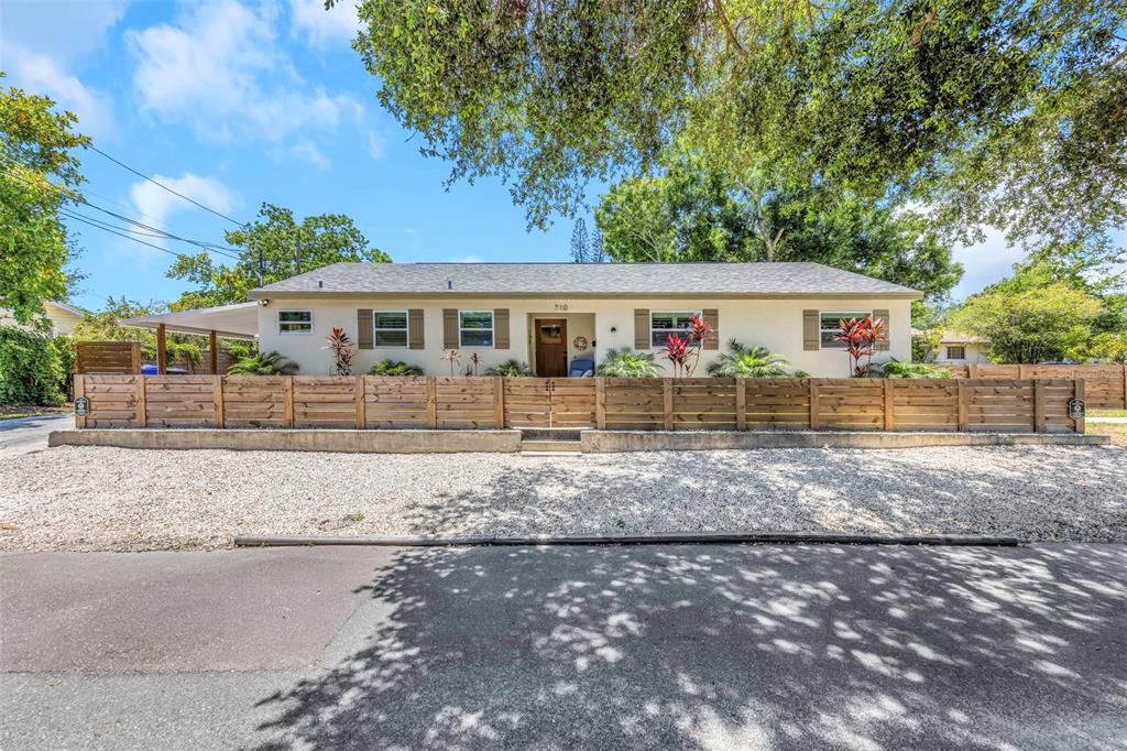 A single-story house with a wooden fence and gravel yard sits under large trees — 710 31ST AVENUE N, ST PETERSBURG, FL