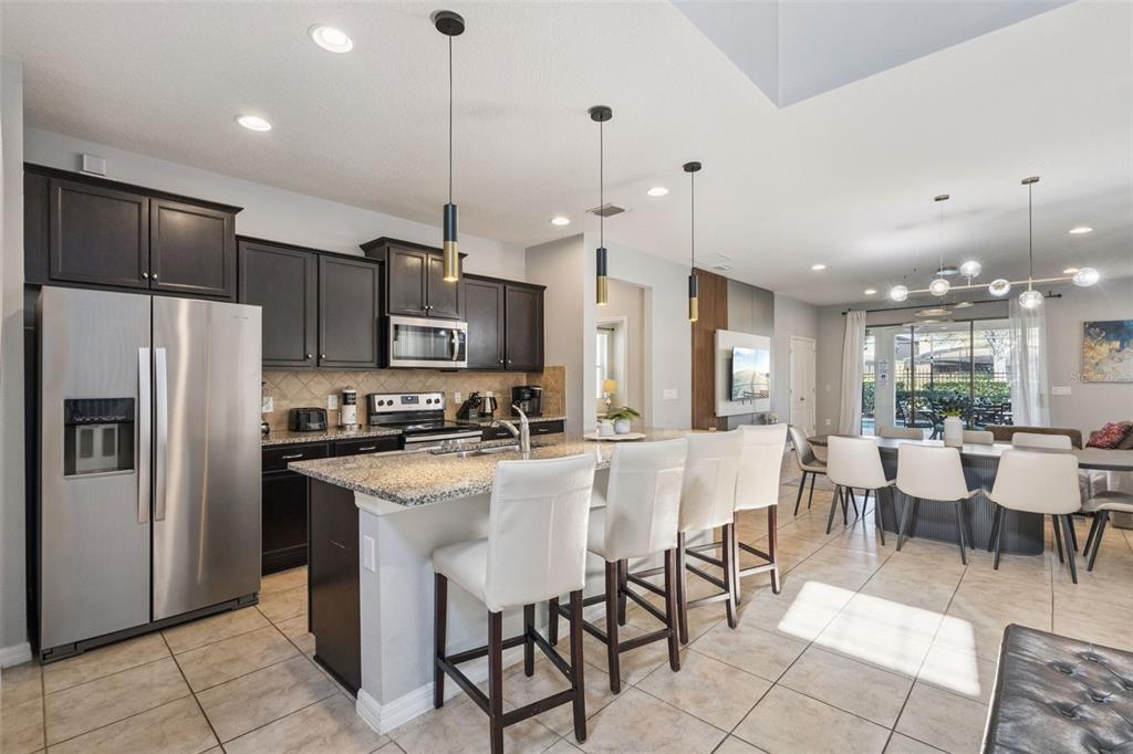 A kitchen with dark cabinets, granite countertops, and a breakfast bar with four white stools — 1844 GOBI DRIVE, KISSIMMEE, FL