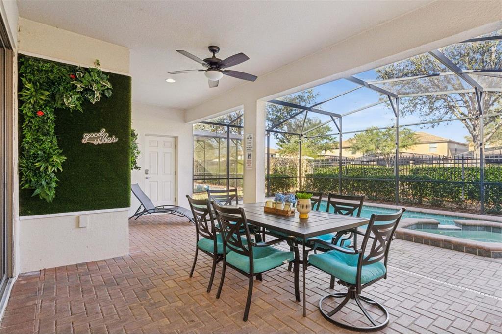 A covered patio features a dining set, a green wall, and a screened-in swimming pool — 1844 GOBI DRIVE, KISSIMMEE, FL