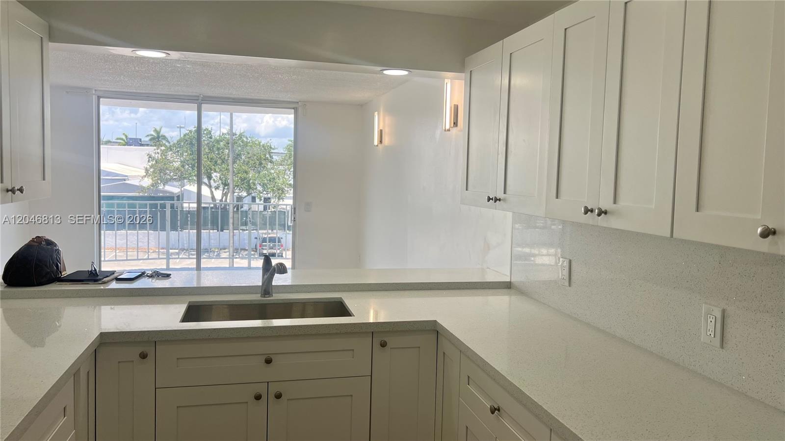 A kitchen with white cabinets, quartz countertops, and a stainless steel sink overlooks a balcony — 488 NW 165th St Rd # 309, Miami FL 33169, MIAMI, FL