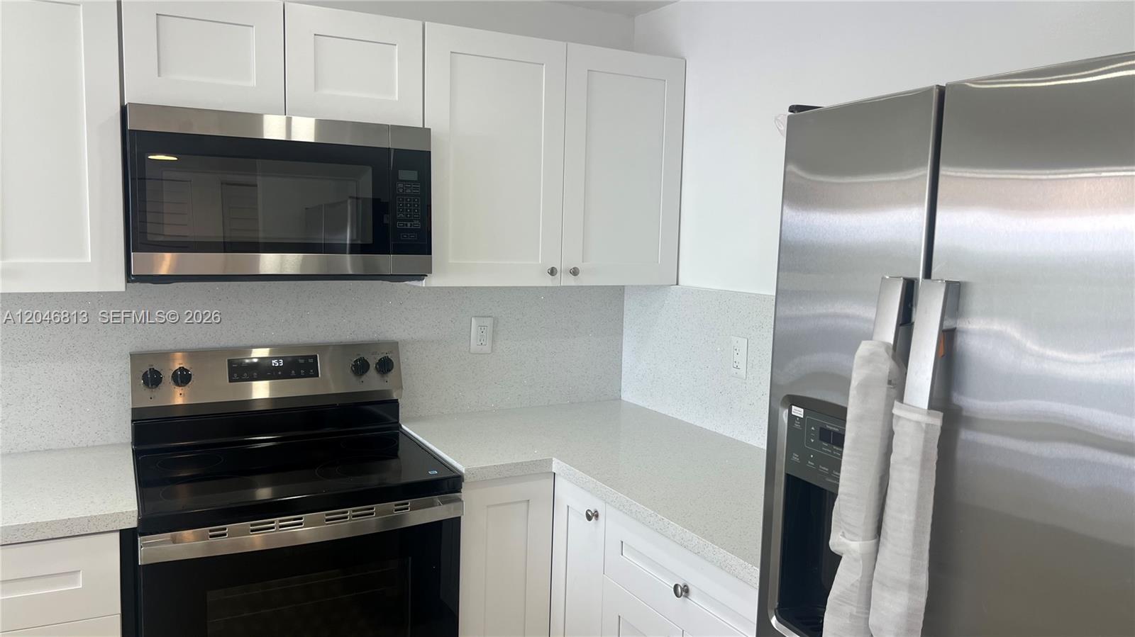 A kitchen features white shaker cabinets, stainless steel appliances, and light-colored speckled quartz countertops — 488 NW 165th St Rd # 309, Miami FL 33169, MIAMI, FL